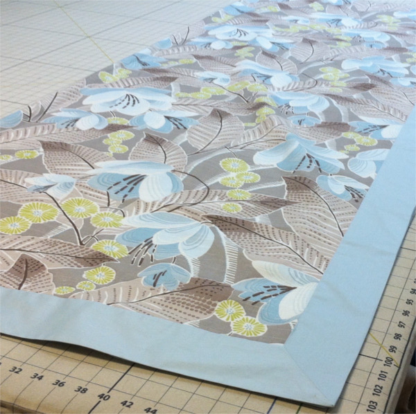 Fabric with flowers and leaves and blue border laid out on cutting table